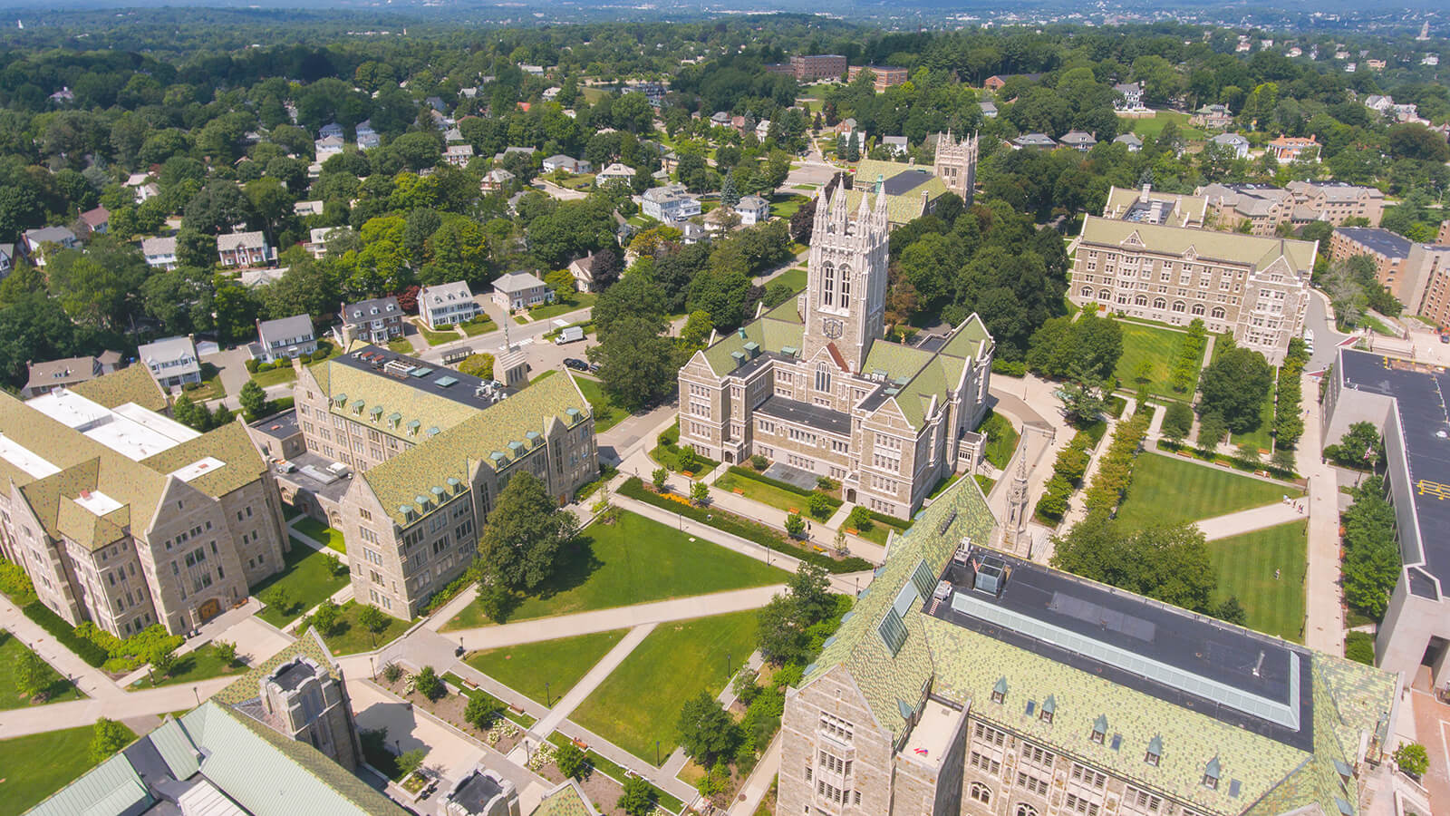 An aerial view of Boston College's sprawling campus. It shows green lawns and multiple college buildings. 