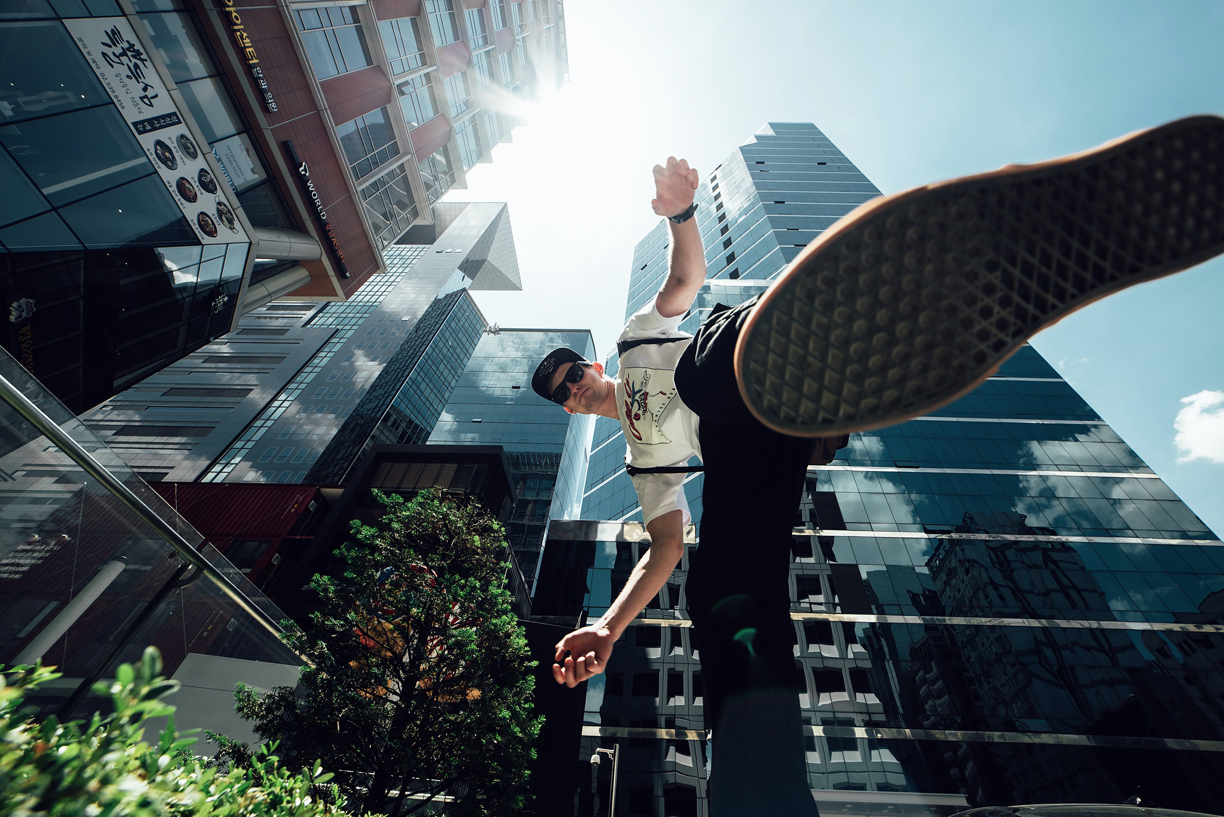 A skyward view of a city with a young man jumping up, over the shot. 
