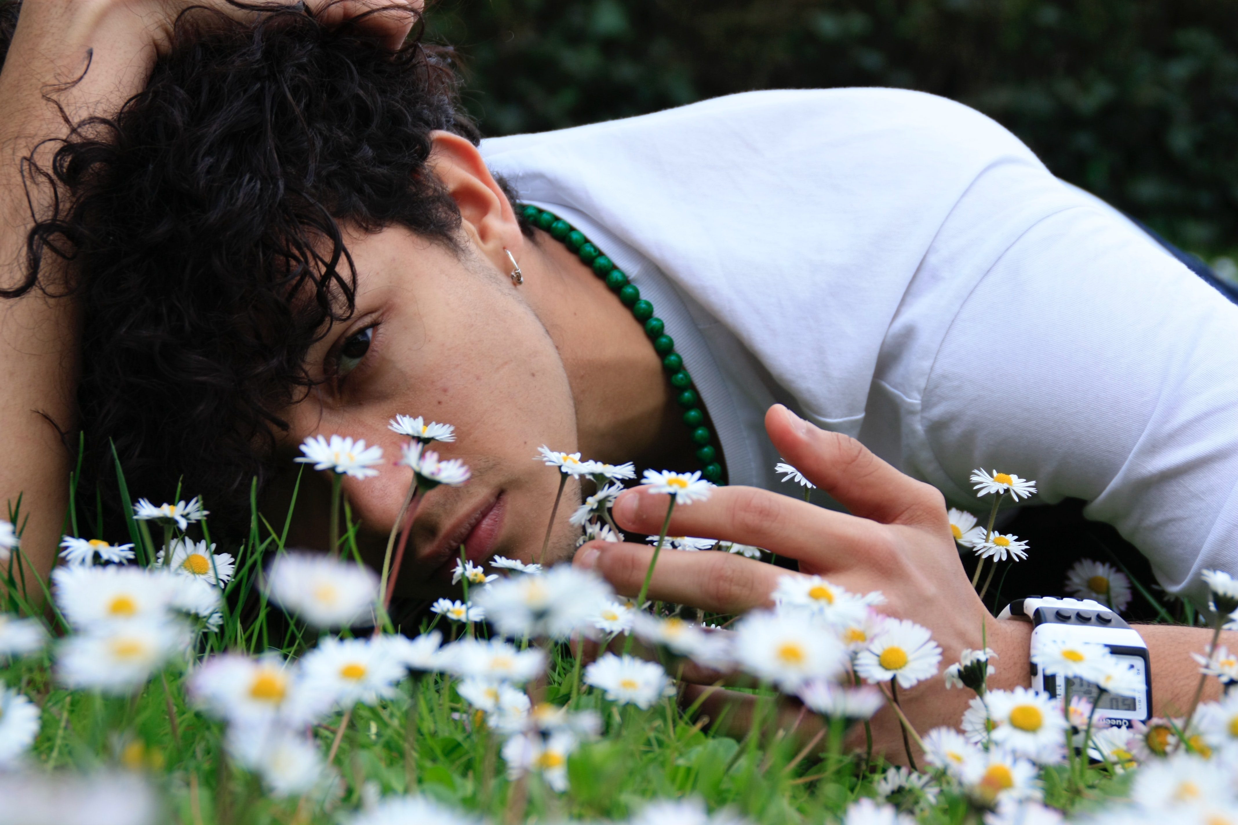 A young man laying in the grass with his face to the camera. There are small white flowers among the green grass blades. 