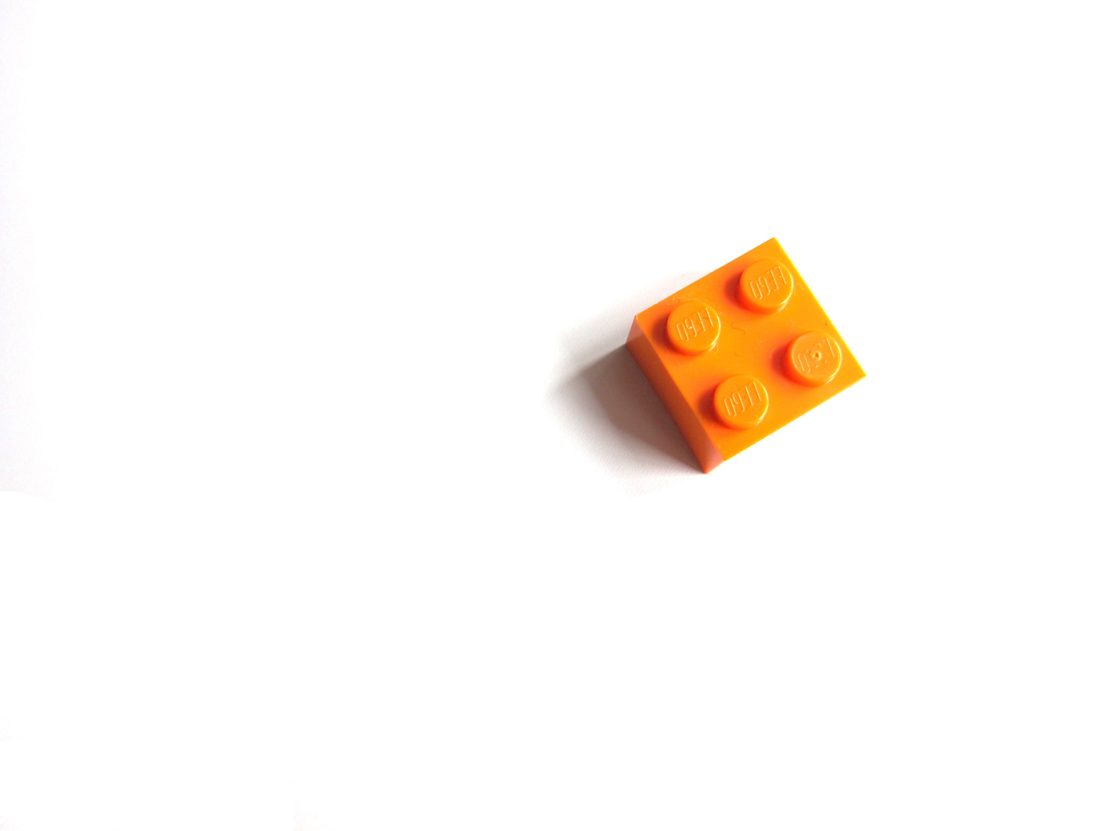 A single, orange lego, face up, sits alone on a white background. 