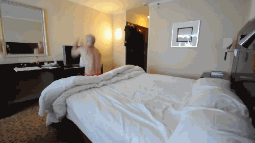 GIF of a boy doing a flip to get into bed under the covers. 