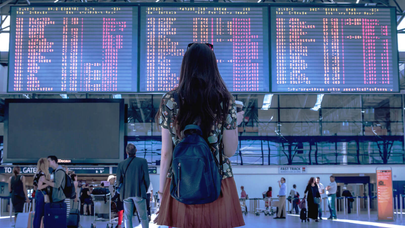 a young woman looks up at a flight tracker board in an airport