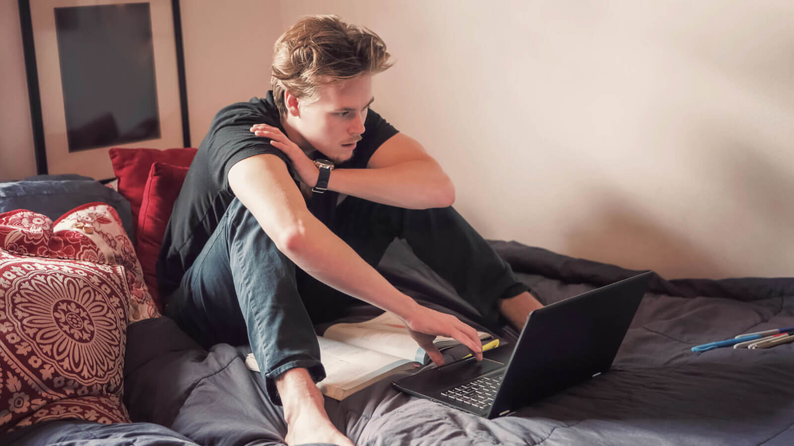 a man sits on his bed looking at his laptop