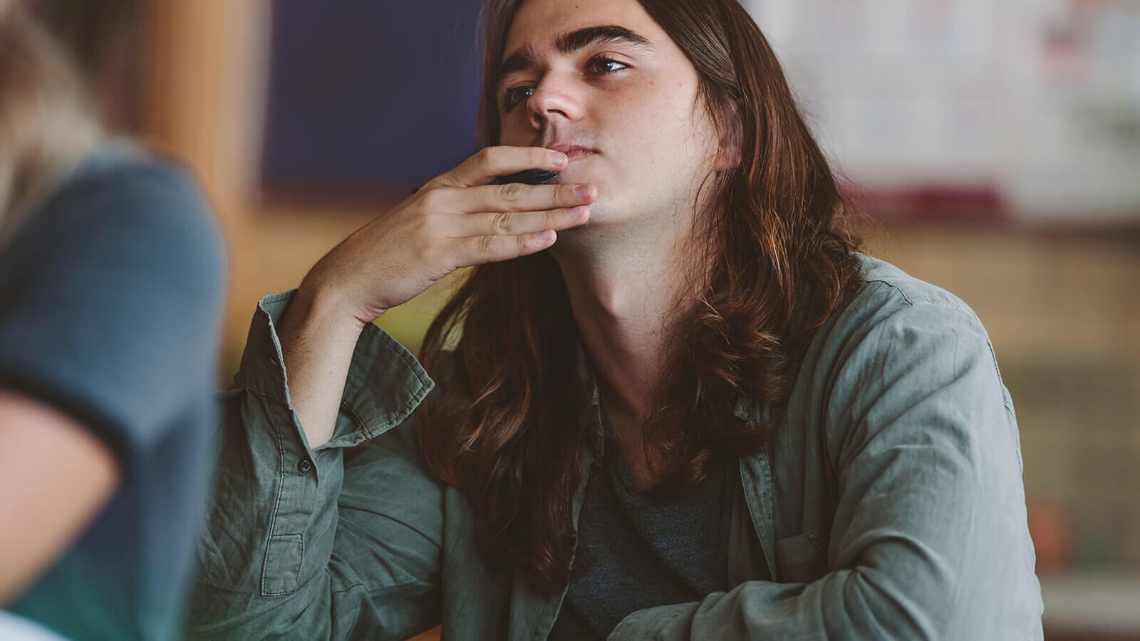 A male student holds his chin and looks off in introspection