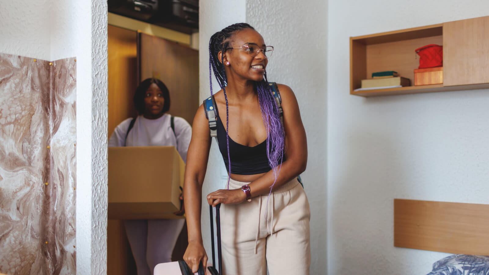 smiling young woman entering dorm room with suitcase