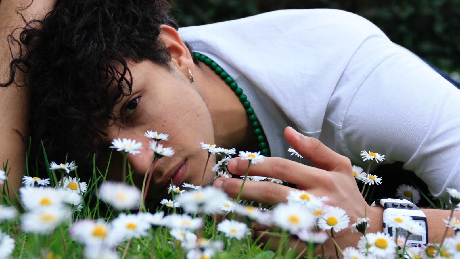 A young man is laying in the grass. There are little white flowers in front of him. 