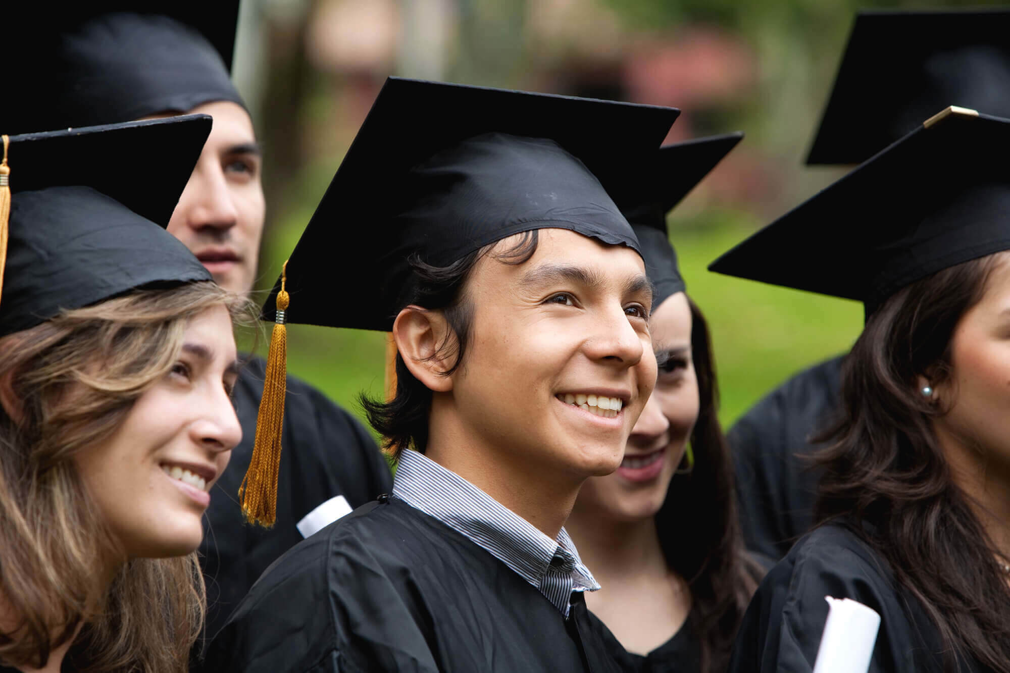 a group of college graduates in black cap and gowns smile