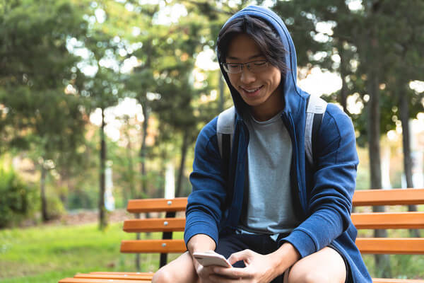 a young man sits on a park bench looking at his phone