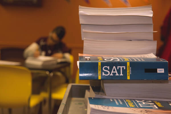 aa stack of SAT test prep books and a student in the background studying