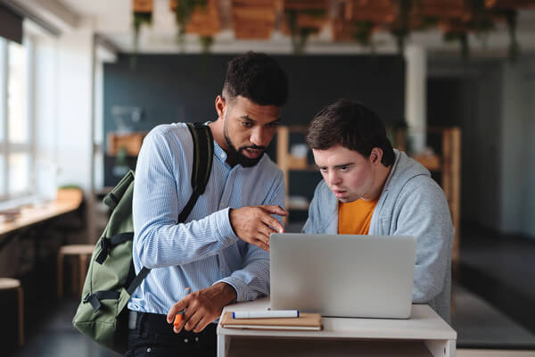 two students work on a laptop in class